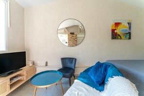 Una sala de estar moderna con una televisión, un espejo redondo, un sofá azul y un cuadro en la pared.