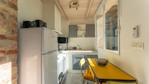 A compact kitchen with a refrigerator, microwave, and sink. There is a yellow table with a chair and a basket.