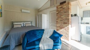 A bedroom with a bed, a blue sofa, a brick wall, and a kitchen area.
