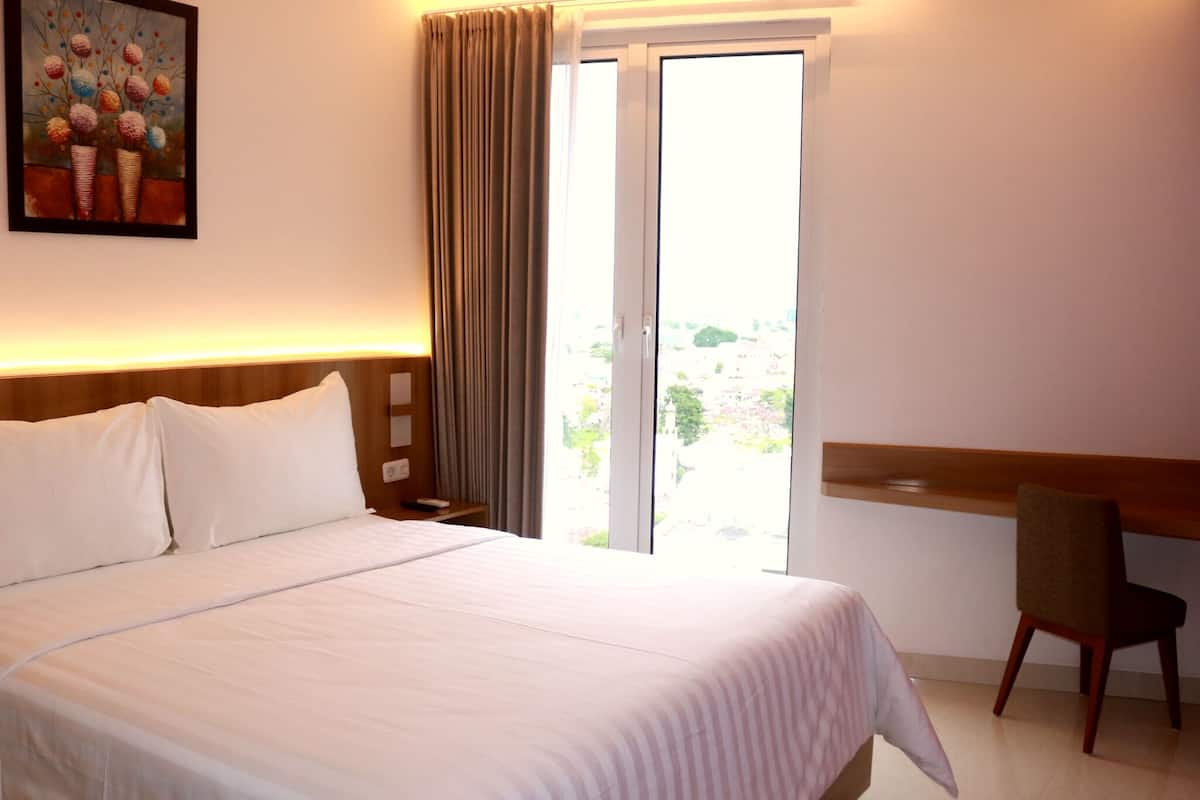 A hotel room with a large bed, a desk, a chair, and a painting on the wall.