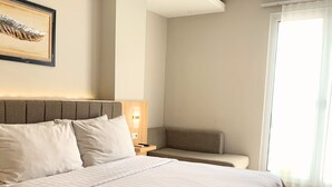 A neatly made bed with a headboard, a bedside table with a lamp, and a window with curtains. - Surabaya River View Hotel (Surabaya)