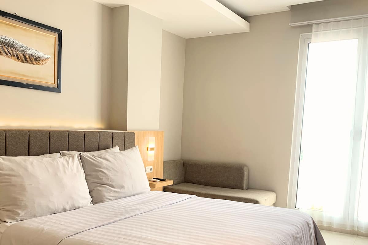A neatly made bed with a headboard, a bedside table with a lamp, and a window with curtains.