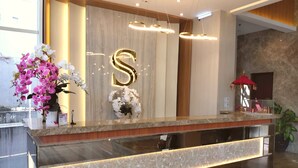 A modern reception desk with a marble countertop, a large illuminated 'S' sign, and a vase of pink orchids. - Surabaya River View Hotel (Surabaya)
