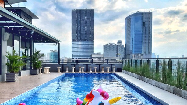 A rooftop pool with a unicorn float, city skyline views, and potted plants. - Surabaya River View Hotel (Surabaya)