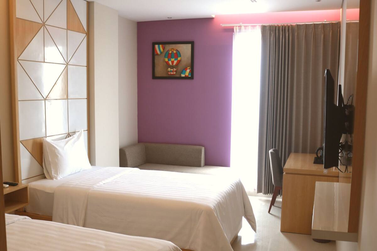 A hotel room with two beds, a sofa, a TV, and a painting on the wall.