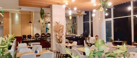 Un interior de restaurante moderno con paneles de techo de madera, luces colgantes y plantas en macetas sobre las mesas.