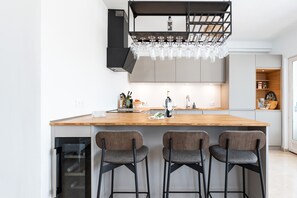 Une cuisine moderne dotée d’un îlot central, de tabourets de bar, d’un meuble à vin et d’un four encastré.