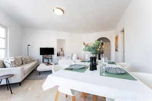 Een moderne woonkamer met een eethoek, witte meubels, een flatscreen televisie en een groene tafelkleed.