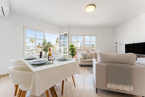 A modern living room with a sofa, a dining table set for two, and a balcony with a view. - Apartment 'Tres Coronas' with Mountain View, Shared Pool and Wi-Fi (Fuengirola)