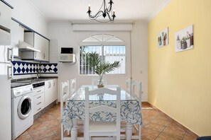 A kitchen with a washing machine, a dining table with chairs, a chandelier, and a window with a view.