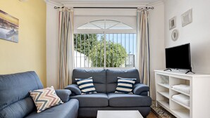 A living room with a grey sofa, a white coffee table, and a TV stand. - Holiday Home "Chalet Fuente3 Shared Pool Family" with Shared Pool and Garden (Conil de la Frontera)