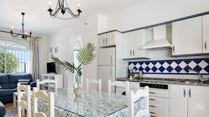 A modern kitchen with white cabinets, a glass dining table, and a blue and white backsplash. - Holiday Home "Chalet Fuente3 Shared Pool Family" with Shared Pool and Garden (Conil de la Frontera)
