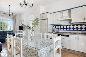 A modern kitchen with white cabinets, a glass dining table, and a blue and white backsplash.