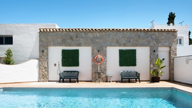 A swimming pool with a stone wall, two chairs, and a lifebuoy. - Holiday Home "Chalet Fuente3 Shared Pool Family" with Shared Pool and Garden (Conil de la Frontera)
