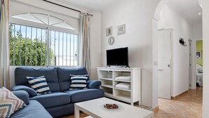 A living room with a sofa, a coffee table, a TV, and a bookshelf. - Holiday Home "Chalet Fuente3 Shared Pool Family" with Shared Pool and Garden (Conil de la Frontera)