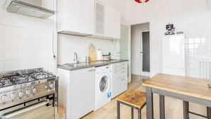 A compact kitchen with a gas stove, a washing machine, and a wooden table. - Apartment in Ancona near Passetto Beach (Ancona)