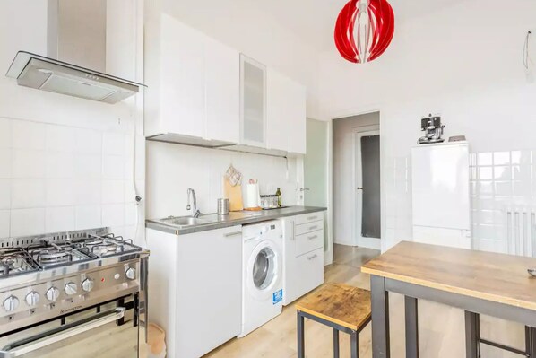 A compact kitchen with a gas stove, a washing machine, and a wooden table.
