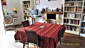 Una sala de estar con una mesa de comedor, sillas, televisor, estanterías y una chimenea.