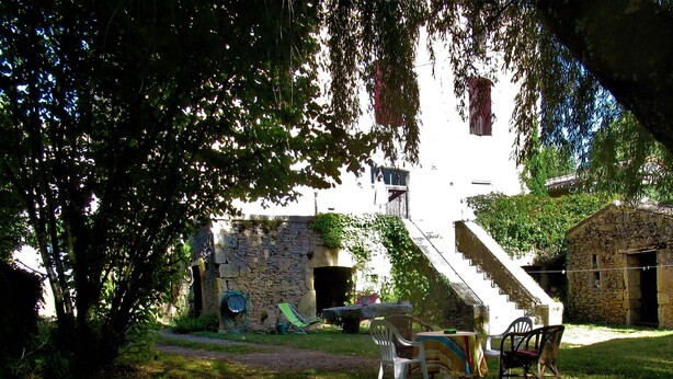 Un edificio de piedra con una escalera que lleva a un segundo piso. Hay zonas de estar al aire libre con sillas y una mesa.
