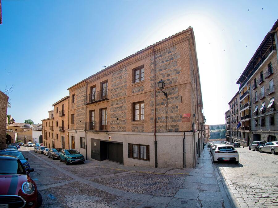 A street with parked cars and a building with a stone facade and multiple windows.