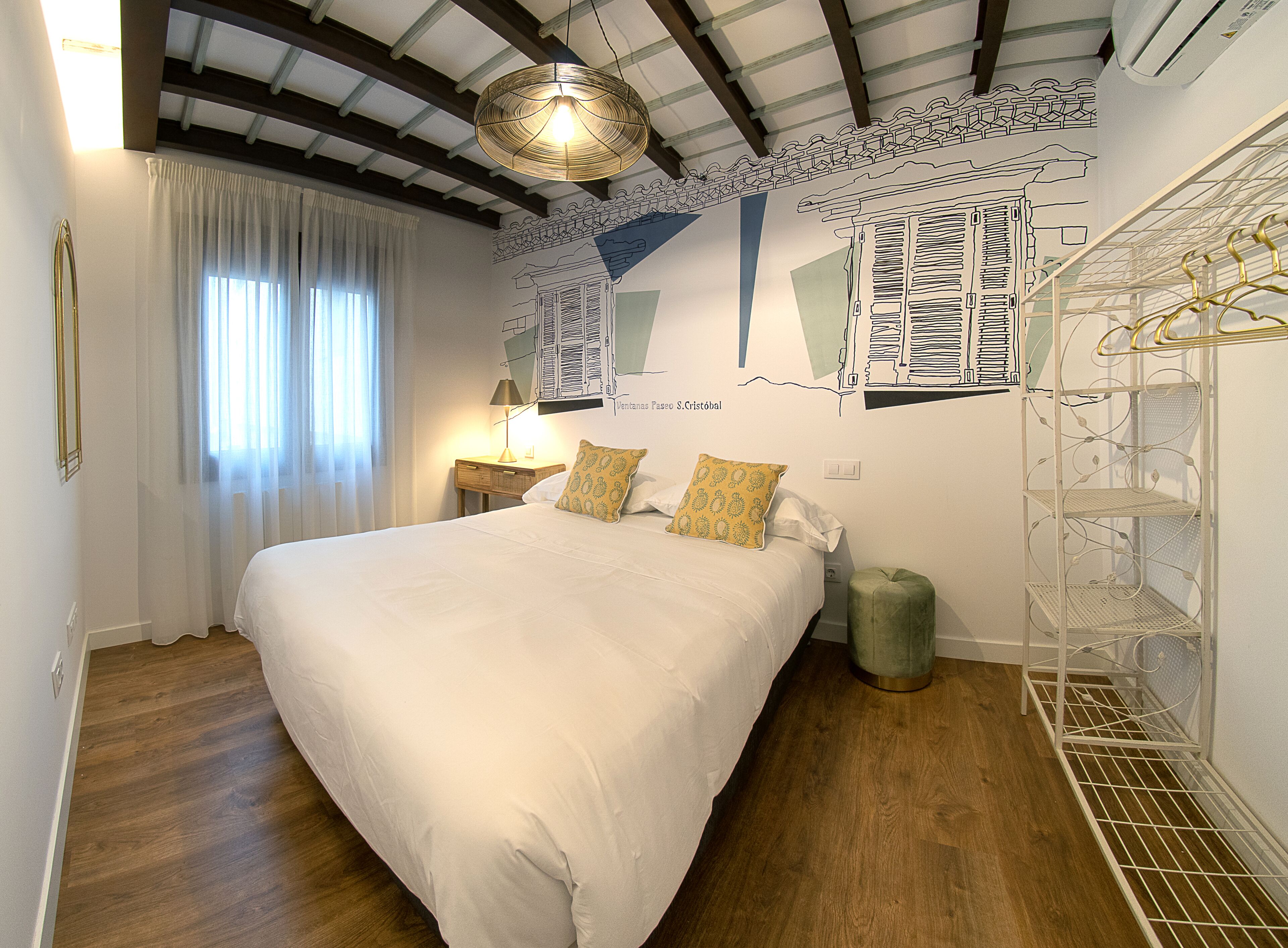 Un dormitorio con una cama grande, una mesita de noche, una lámpara, un reposapiés verde y un estante en la pared.