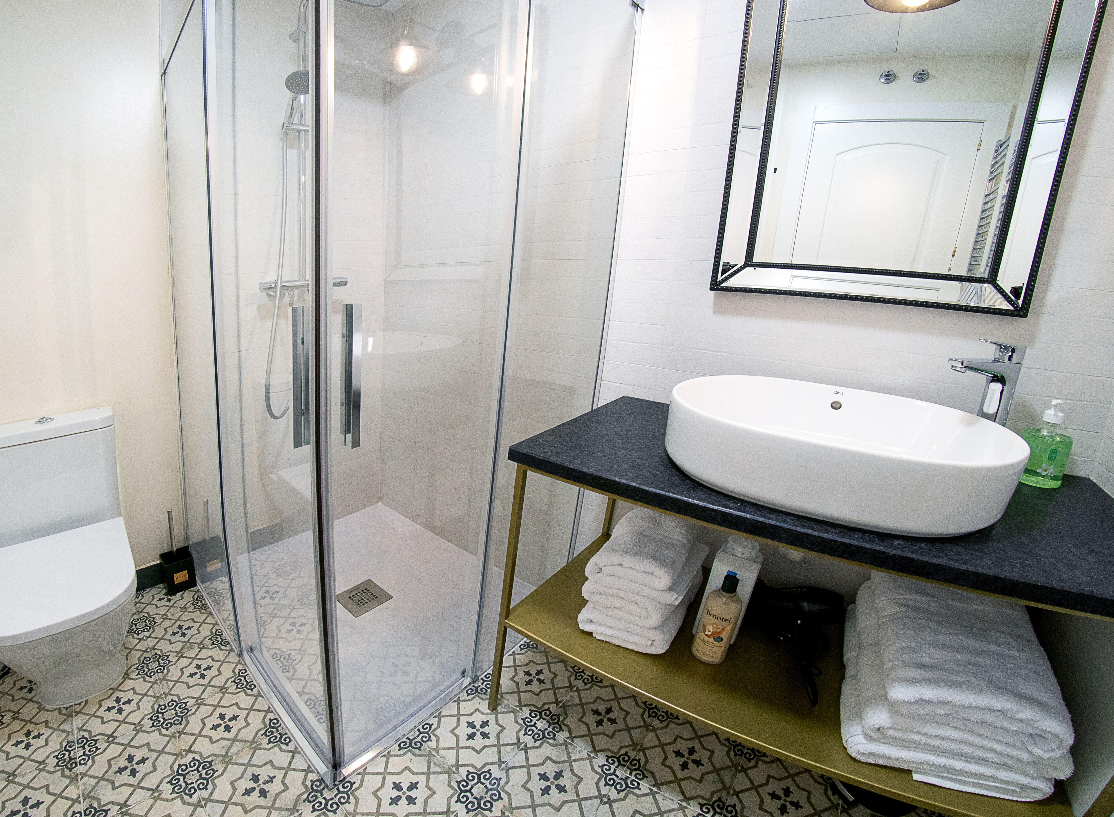 A bathroom with a glass-enclosed shower, a white sink, and a black countertop.