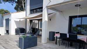 An outdoor patio with a seating area, a planter with plants, and a table with chairs.