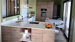 A modern kitchen with a central island, built-in oven, and a dining area with white chairs.