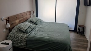 A bedroom with a bed, a nightstand, a lamp, a speaker, and a sliding door.