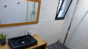 A bathroom with a wooden vanity, a black sink, a mirror, a small potted plant, and a shower area with a checkered floor.
