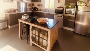 Une cuisine moderne dotée d’un îlot central, d’appareils électroménagers en acier inoxydable et d’un luminaire suspendu.