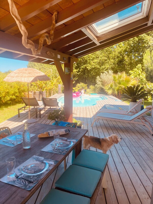 Una terraza exterior con mesa de comedor, sillas de salón y piscina.