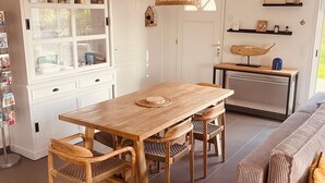 Un vaste espace de vie comprenant une table à manger en bois, des chaises en osier, un canapé et un luminaire suspendu.