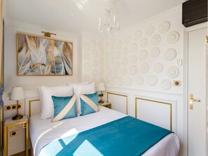 Una habitación de hotel con cama, candelabro, un cuadro y paneles decorativos en la pared.