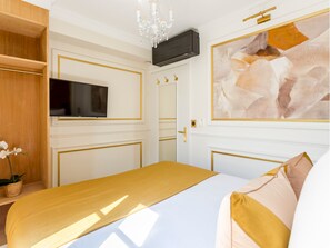 A hotel room with a bed, a television, a chandelier, and a painting on the wall.
