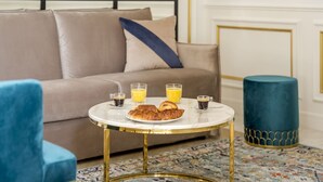 A cozy living area with a sofa, a round coffee table with breakfast items, and a blue accent chair. - Merveil - Luxury Suite - Tour Eiffel - Bac I (Paris)