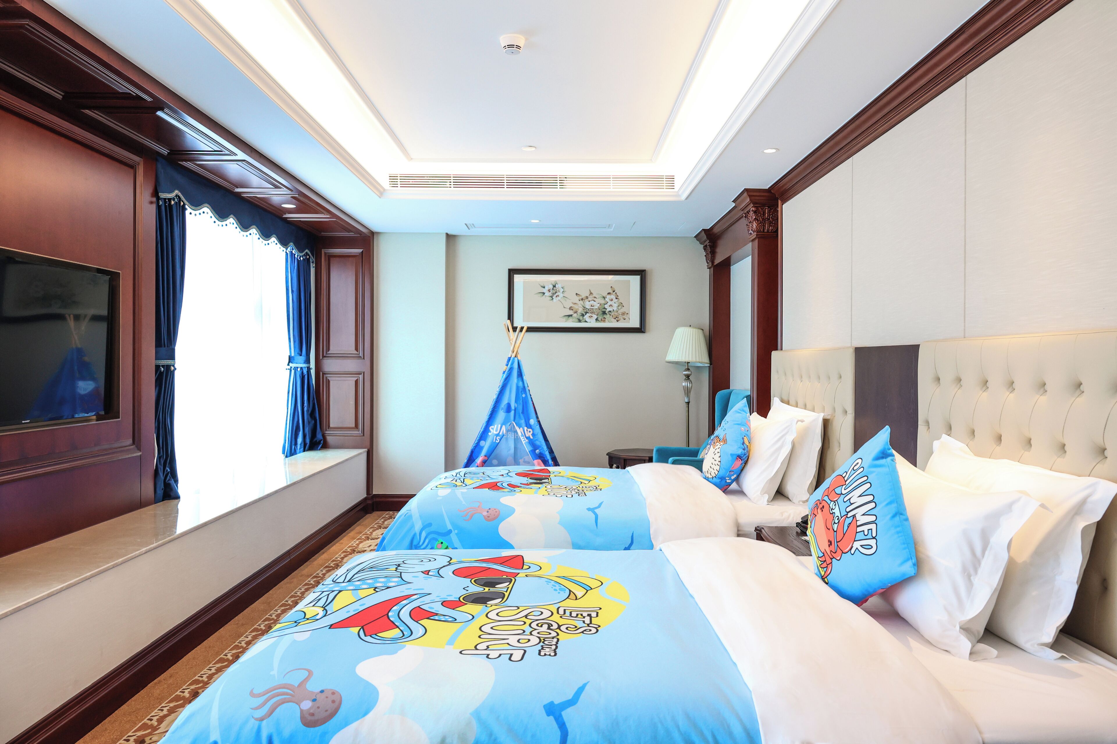 A hotel room with two beds, a large window, a flat-screen TV, and a ceiling fan.
