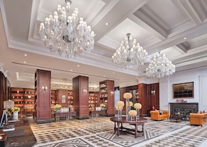 Eine geräumige Lobby mit Schachbrettmuster-Boden, großen Kronleuchtern, Holzregalen und einem Kamin.