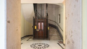 Un magnifique escalier orné d’une rampe en métal décorative, une porte en bois avec une poignée en laiton et un sol en marbre présentant un motif géométrique.