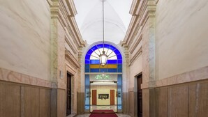 Un vaste hall d’entrée avec un plafond haut, une grande rosace centrale en verre coloré bleu et un tapis rouge menant à un espace de réception.