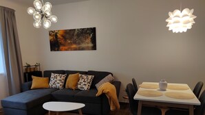 A modern living room with a sectional sofa, a round coffee table, a dining table with chairs, and a large abstract painting on the wall. - New apartment in the quiet of the Jizera Mountains (Smržovka)