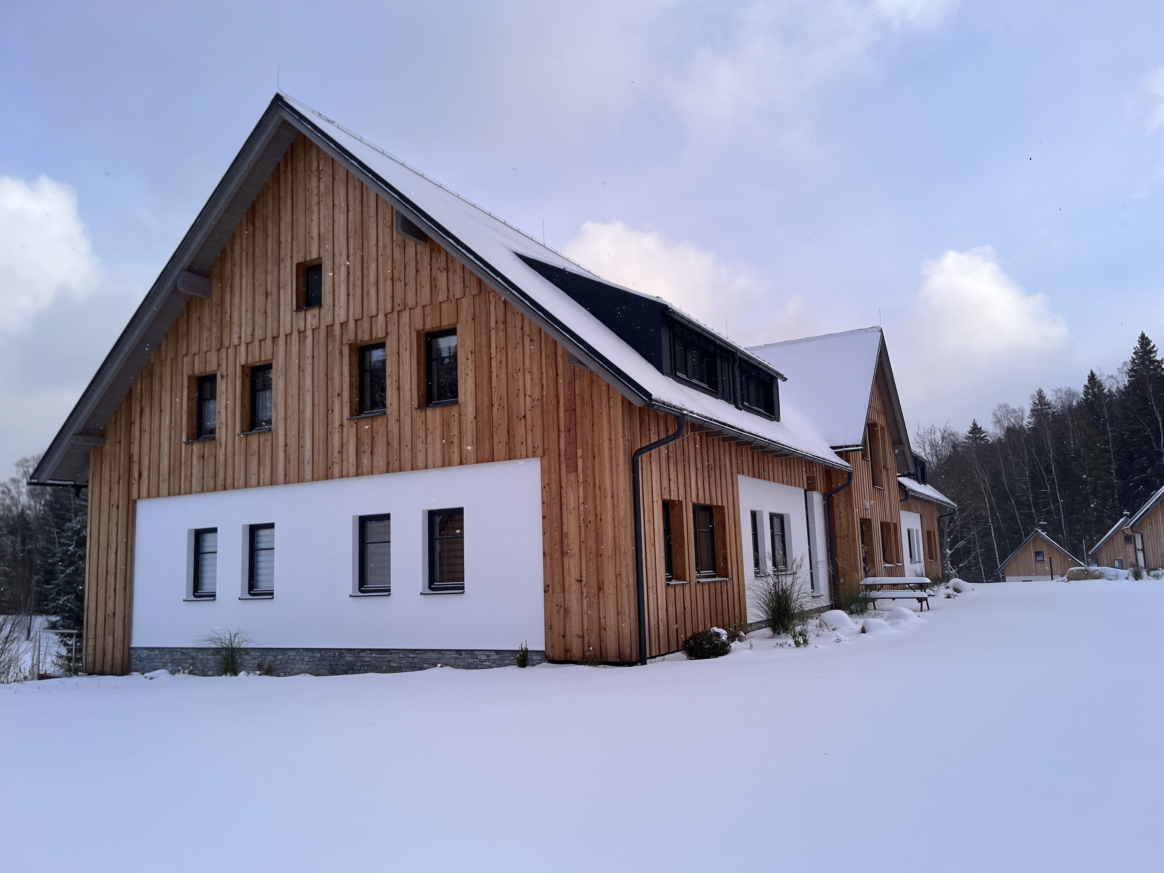 A wooden building with a sloped roof and multiple windows, surrounded by snow.