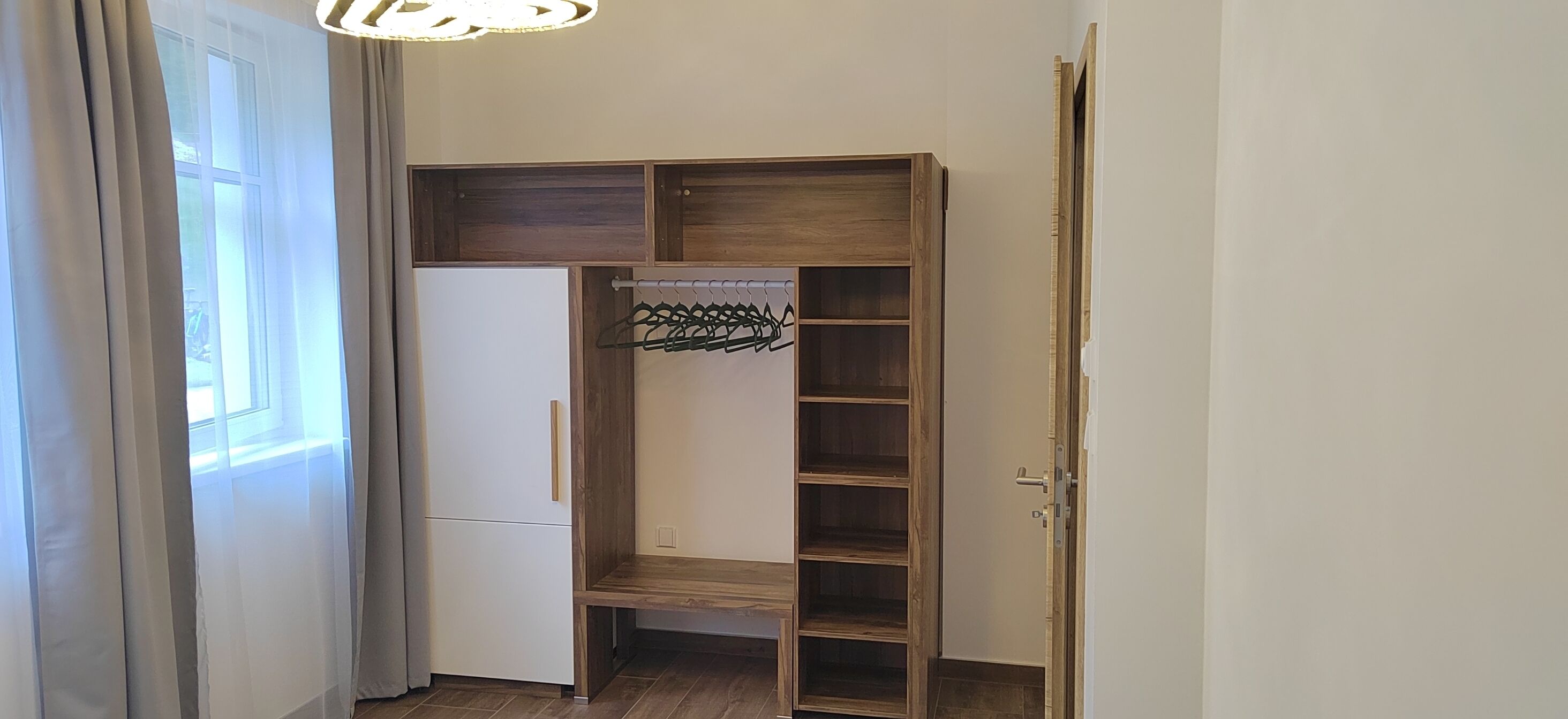 A room with a wooden wardrobe, a white refrigerator, and a door with a handle.