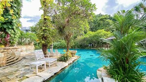 A pool area with stone steps, lounge chairs, and lush greenery. - Lorin Solo Hotel (Colomadu)