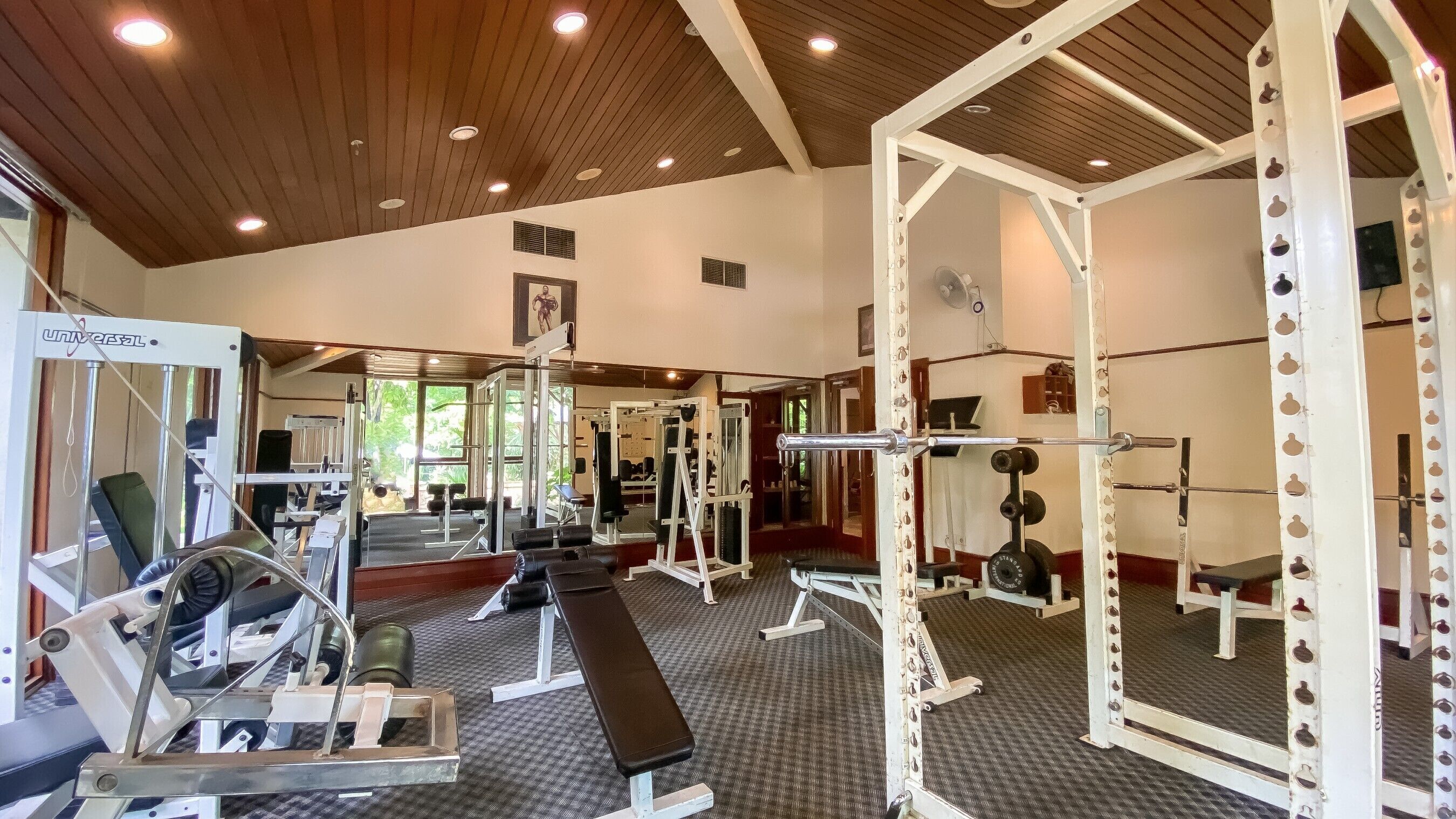 Une salle de sport équipée de divers appareils d’entraînement, notamment des machines à poids et des poids libres, et dont les murs sont recouverts de miroirs.