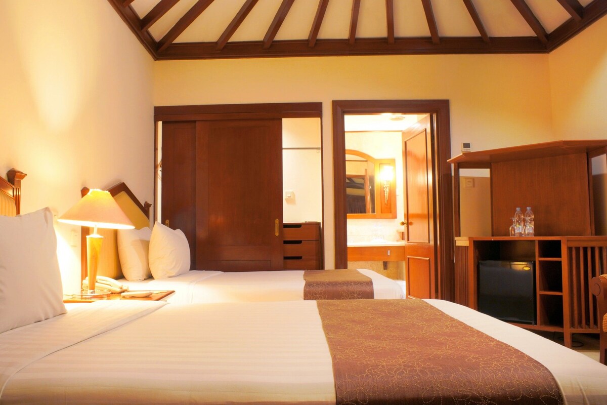 A hotel room with two beds, a desk, a chair, and a television.