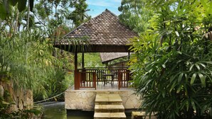 Ein Gazebo mit einem Ziegeldach, umgeben von üppiger Vegetation und einem kleinen Wasserspiel.