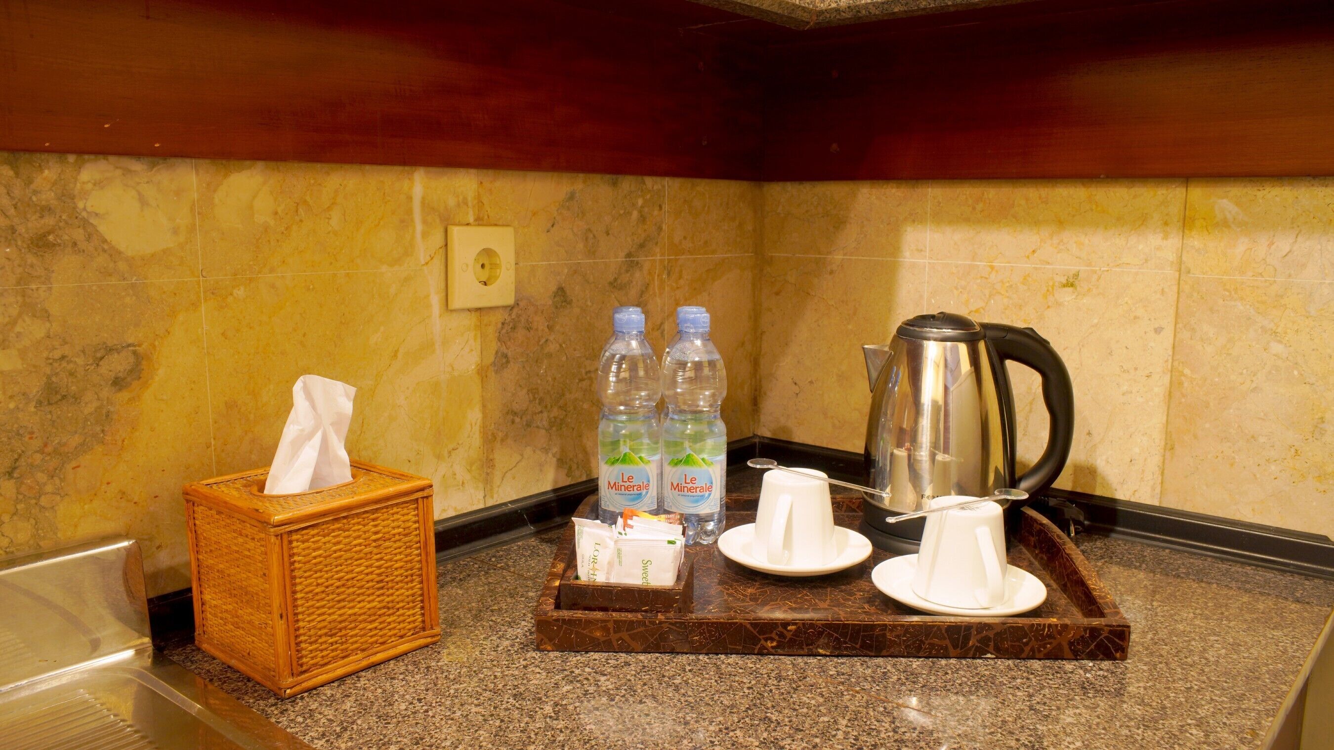 Un angolo cottura in hotel con un pacco di fazzoletti, due bottiglie d'acqua, una caffettiera e un vassoio con un misurino di zucchero e un contenitore per latte.