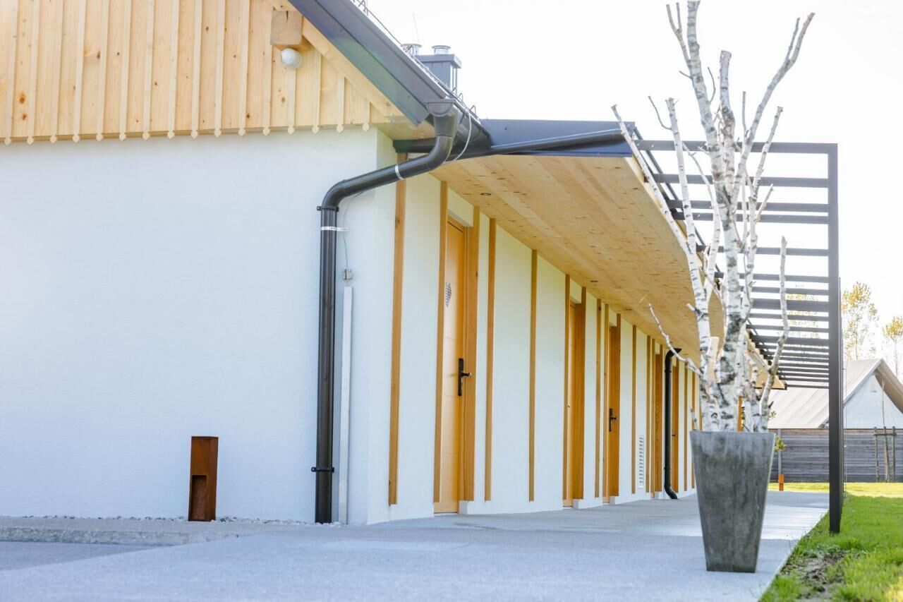 Ein modernes Gebäude mit Holzfassade, einem überdachten Gang und einem großen Pflanzkübel mit einem Baum.