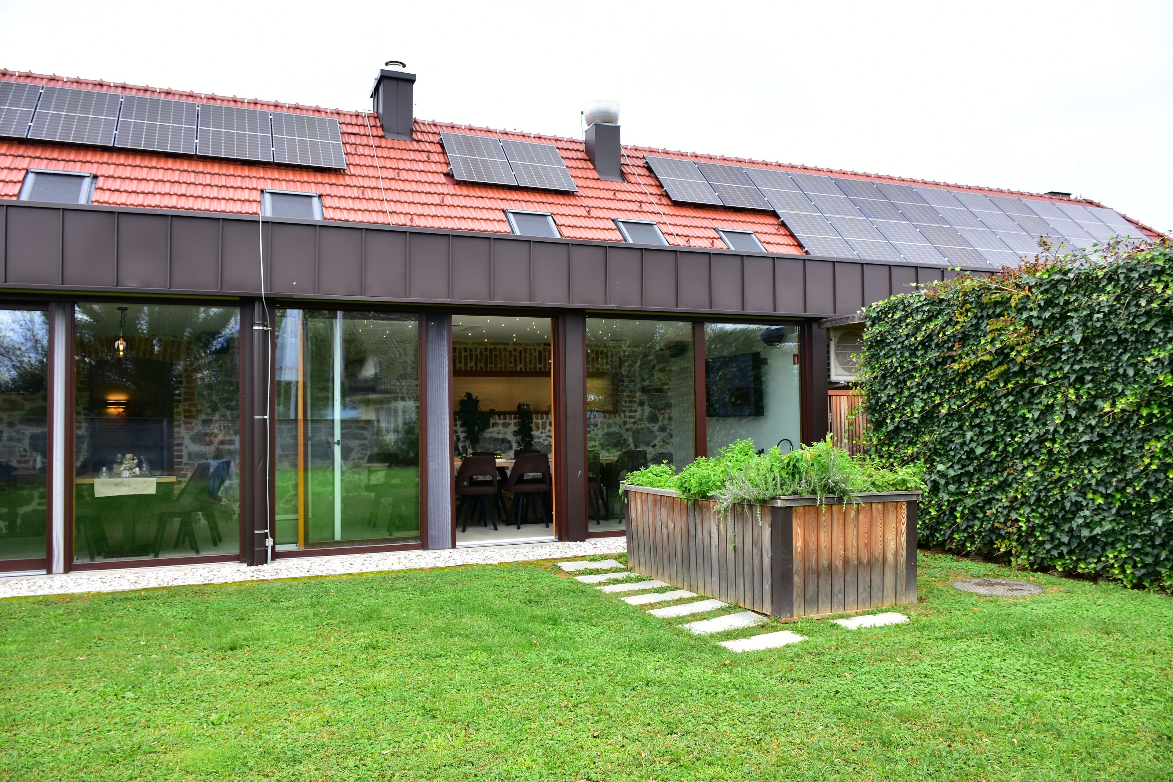 Una casa moderna con techo de tejas rojas, amplios ventanales y paneles solares.